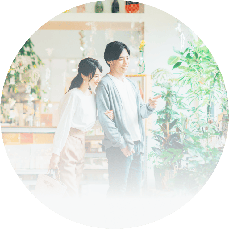 観葉植物が並ぶ明るい店内で、若い男女が並んで歩きながら商品を見ている人物写真